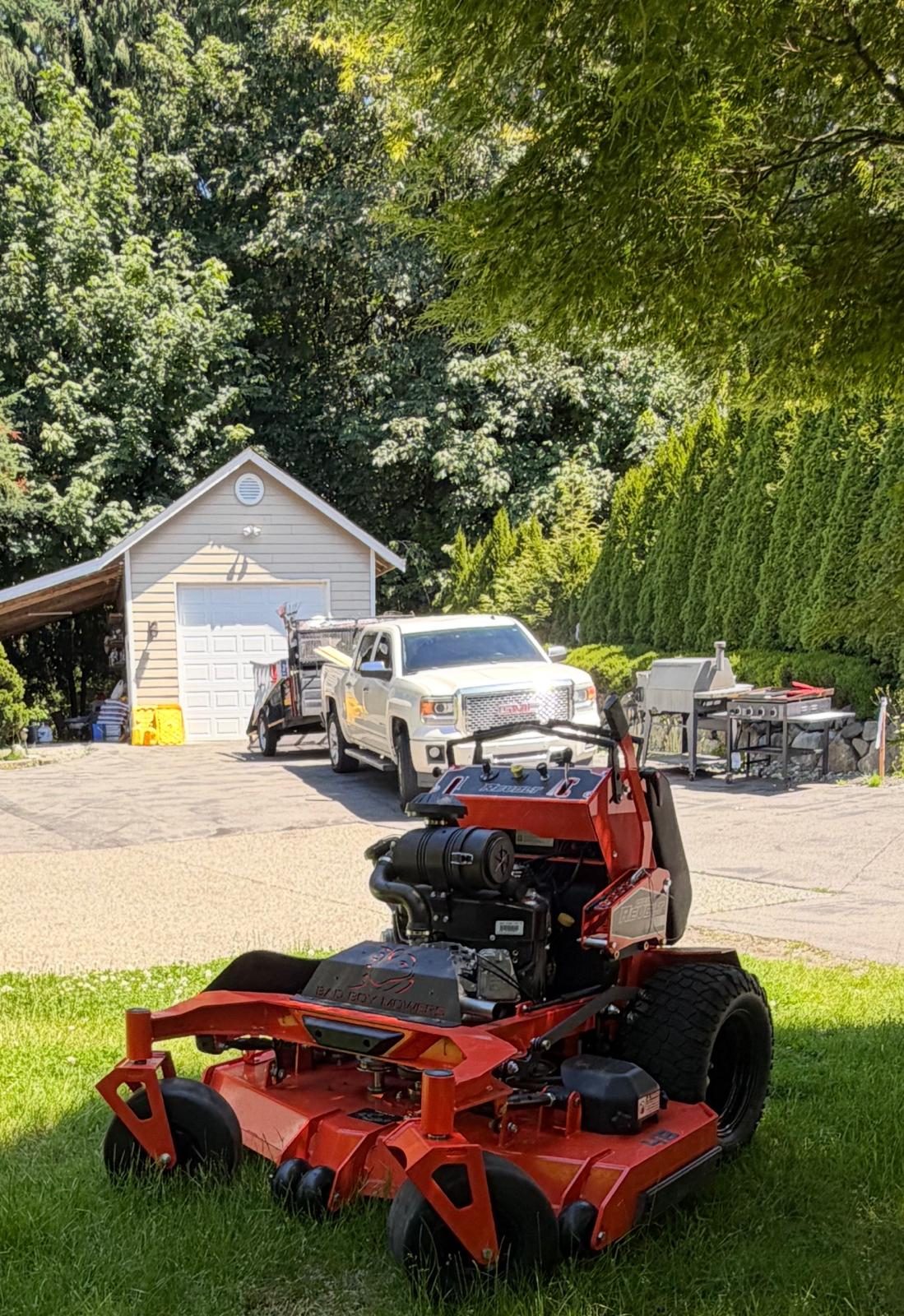 1st Choice Landscaping stand-on mower with the work truck and shop behind it